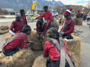Gruppenspieler in roten Shirts sitzen auf Heuballen und bereiten sich auf einen Auftritt vor.